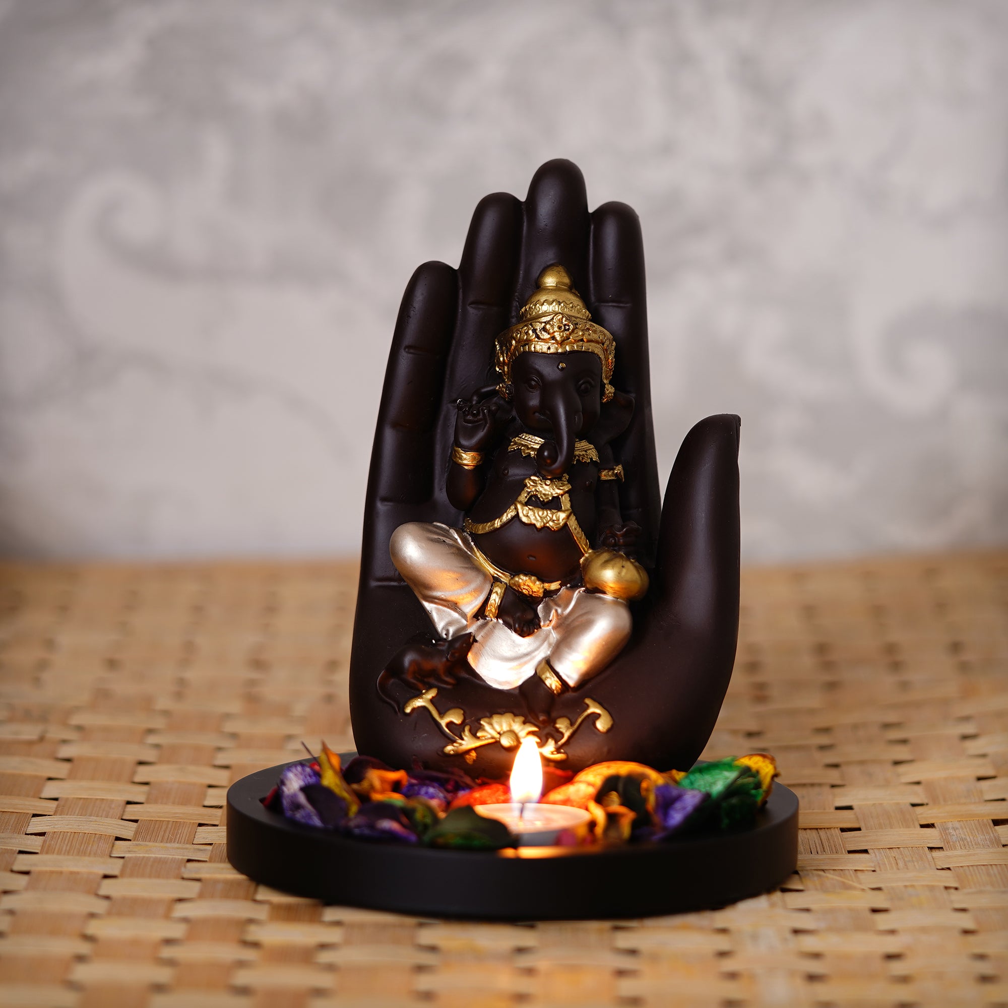 Golden and Black Handcrafted Palm Ganesha Idol on Wooden Base with Fragranced Petals Tealight Candle Holder
