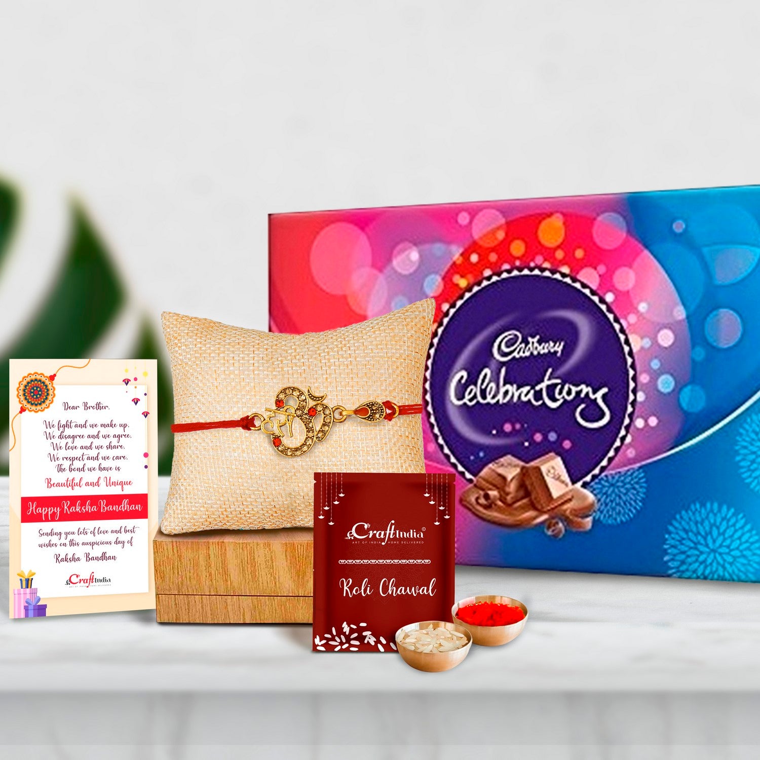 Designer Om Rakhi with Cadbury Celebrations Gift Pack of 7 Assorted Chocolates and Roli Chawal Pack, Best Wishes Greeting Card
