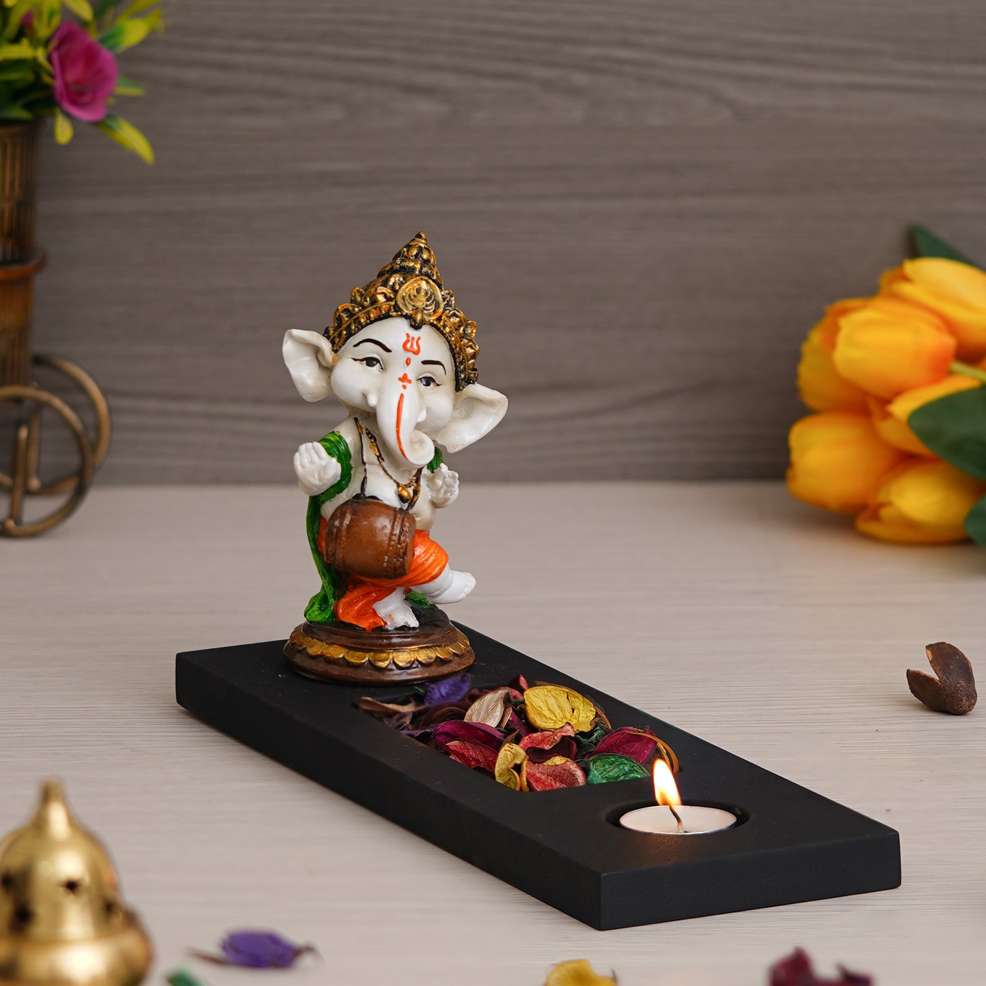 Orange, Brown, White & Black Polyresin Baal Ganesha Playing Dholak Showpiece with Rectangle Wooden Base, Fragranced Petals & Tealight